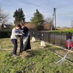 Dwóch chłopców, jeden trzyma duży worek, drugi wsypuje do niego liście