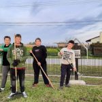 Czterech chłopców, każdy trzyma w ręce grabie. Porządkują smentarz wojskowy