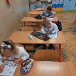 Czworo uczniów siedzi w ławkach, wszyscy kolorują obrazki