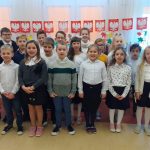 Grupa uczniów ubranych na galowo stoi na baczność wykonując hymn państwowy