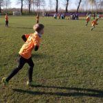 Chłopiec w pomarańczowej koszulce biegnie po boisku, w tle widać pozostałych zawodników