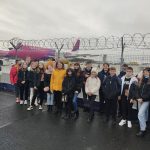 Zdjęcie grupowe wycieczkowiczów na lotnisku. W tle samoloty