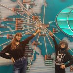 Dwie dziewczynki ubrane na czarno stoją przed mapą lotnisk, wskazują palcami napis: Krakow Airport