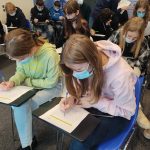 Dwie uczennice rozwiązują krzyżówkę związaną z lotniskiem, za nimi grupa uczniów pochylonych nad kartami pracy