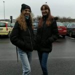 Dwię uśmiechnięte dziewczynki na parkingu samochodowym, w tle samochody