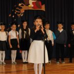 Dziewczynka w białej spódnicy i czarnej bluzce recytuje wiersz do mikrofonu