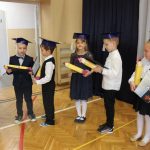 Siedmioro dzieci stoi na sali gimnastycznej, w rękach trzymają duże kredki z kartonu