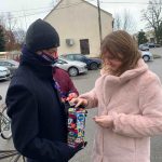 Uśmiechnięta dziewczynka w różowym futerku wrzuca pieniądze do puszki, którą trzyma chłopiec w czarnej czapce i płaszczu.