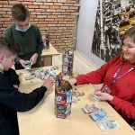 Dwóch chłopców i dziewczynka siedzą przy stoliku, liczą pieniądze. Na stoliku stoją dwie puszki WOŚP, oraz leżą zebrane pieniądze