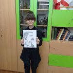 Uśmiechnięta dziewczyna trzyma w rękach portret Piłsudskiego. W tle szklana szafka z eksponatami z II wojny światowej