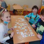 Troje dzieci siedzi przy stoliku, na nim rozłożone karteczki z produktami.