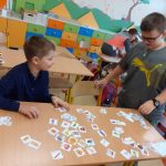 Dwóch chłopców przy ławce z rozłożonymi karteczkami produktów.