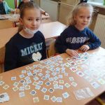 Dwie dziewczynki siedzą przy stoliku, na nim obrazki produktów i pieniążków.