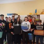 Grupa uczniów w czarnych i żółtych koszulkach stoi przed regałem