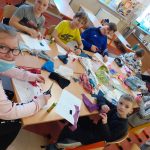 Grupa uczniów siedzi przy stole, projektuje stroje. Na stole potrzebne materiały.