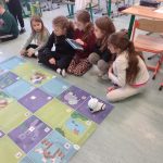 5 dziewczynek patrzy na tablet ,jedna dziewczynka trzyma w ręku tablet ,photon stoi na planszy przed dziewczynkami.