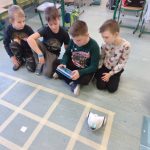 Czterech chłopców siedzi na podłodze, jeden chłopiec trzyma w ręku tablet,trzech chłopców patrzy na tablet. Na podłodze stoi Photon.
