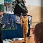 Chłopiec trzyma kukiełkę czarownicy na tle sceny.