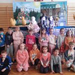 Uczniowie klas pierwszych stoją na tle sceny z kukiełkami.