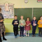 Pięcioro uczniów i kobieta stoją na tle tablicy, trzymając w dłoniach czekolady.