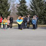 Uczniowie stoją w rzędach na boisku, jeden z nich trzyma wielkie, niebiesko - żółte serce