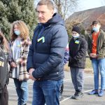 Mężczyzna w granatowej kurtce z przypiętą niebiesko - żółtą wstążeczką. Za nim dwóch chłopców i dziewczyna.