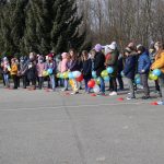 Duża grupa uczniów stoi na boisku, w rękach wszyscy trzymają żółte i niebieskie balony