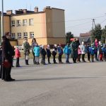 Na boisku przed szkołą stoi ksiądz, wokół niego ustawieni w szeregu uczniowie