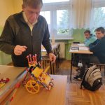 Nauczyciel prezentuje kolorowy model urządzenia napędzanego strumieniem wody lub innego czynnika zbudowany z klocków