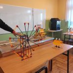 Kolorowy model wiatraka zbudowany z klocków. W tle biała tablica ścienna i czarna drukarka 3D