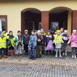 Dzieci stoją na tle szkoły z workami pełnymi śmieci.