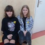 Dwie dziewczynki siedzą na ławce, na bluzkach mają papierowe, żółte żonkile