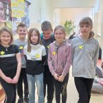 Uczniowie klasy 4, cztery dziewczynki i dwóch chłopców, prezentują na szkolnym korytarzu żółte żonkile przypięte do ubrania