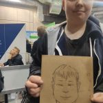 Chłopiec trzyma w ręce swoją karykaturę wykonaną przez uczniów prezentujących liceum plastyczne