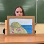 Dziewczynka siedzi w ławce, czyta tekst. Przed nią stoi teatrzyk z obrazkiem