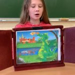 Dziewczynka czyta opowieść. Na stojącej przed nią ilustracji smok wawelski