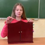 Dziewczynka w różowym swetrze otwiera drzwiczki drewnianego teatrzyku