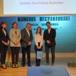 Trzy kobiety, dwóch mężczyzn i dzieczynka stoją uśmiechnięci na scenie