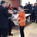 Chłopiec w pomarańczowej koszulce odbiera nagrodę od mężczyzny