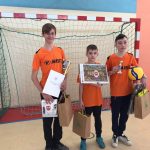 Trzej chłopcy stoją przed bramką do piłki nożnej, trzymają dyplomy 9 nagrody