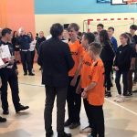 Trzech chłopców w pomarańczowych koszulkach odbiera gratulacje od organizatora konkursu