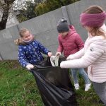 Trzy dziewczynki, dwie trzymają worek, jedna wrzuca zebrane śmieci