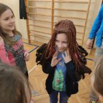 Uśmiechnięta dziewczynka w niebieskiej bluzce w bordowej peruce.