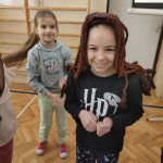 Uśmiechnięta dziewczynka w czarnej bluzie z białym napisem w bordowej peruce.