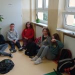 Trzy dziewczynki i jeden chłopiec z klasy 8a siedzą na korytarzu. Ich bluzy ozdobione są żółtymi żonkilami.