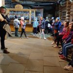 Grupa dzieci słuchająca kobiety, która trzyma tekst wiersza na karcie.