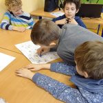 Chłopiec w szarym dresie przesuwa pionek po mapie miasteczka żydowskiego, trzech innych chłopców przygląda się.