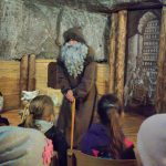 Starszy pan o lasce stojący przed grupą siedzących dzieci.