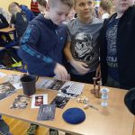 Trzech chłopców z klasy 4 ogląda przedmioty rozłożone na stoliku. Wśród nich jest kubek dwuuchy, drejdle, jad, kielich.