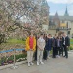 Grupa uczniów pod kwitnącym drzewem, w tle zamek